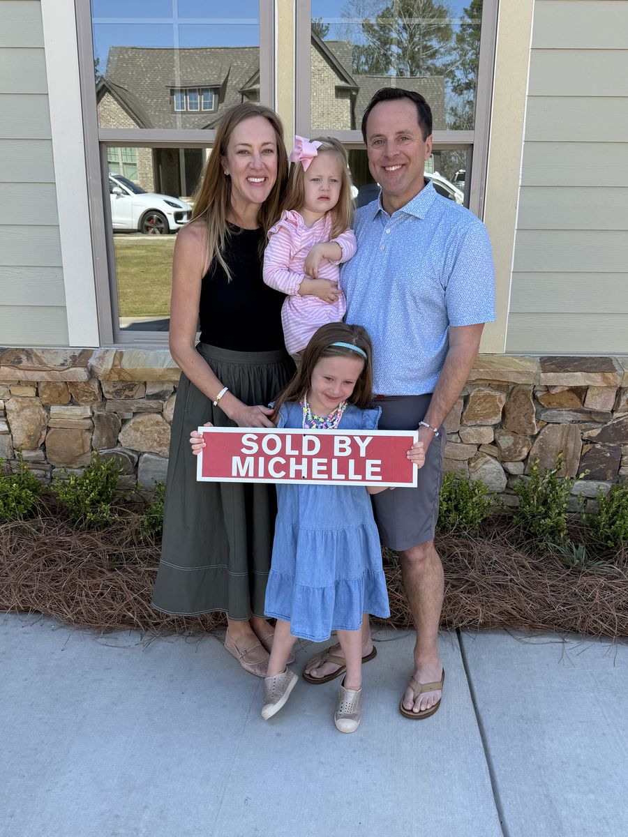 Michelle&rsquo;s clients, a family with two children, holding a Sold by Michelle sign outside their home
