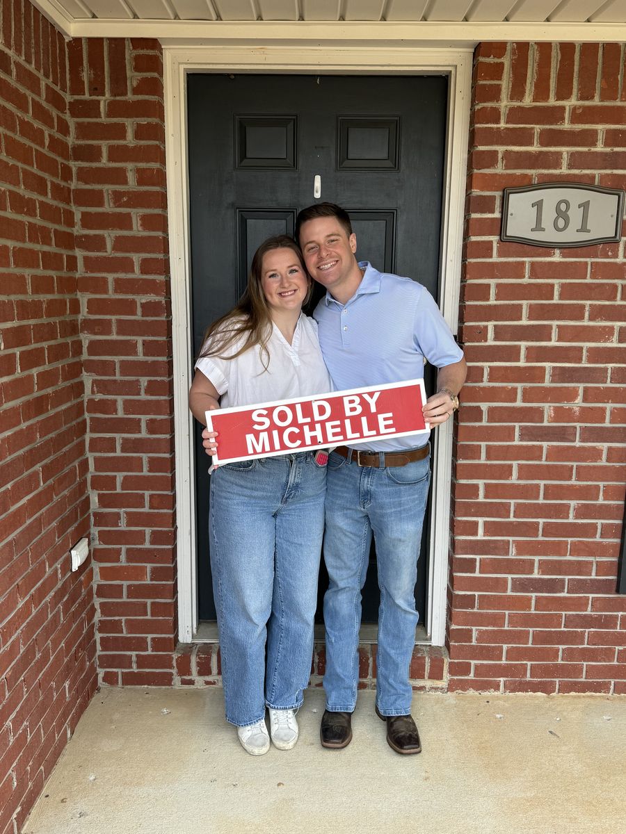 Michelle&rsquo;s clients holding a Sold by Michelle sign outside a brick home
