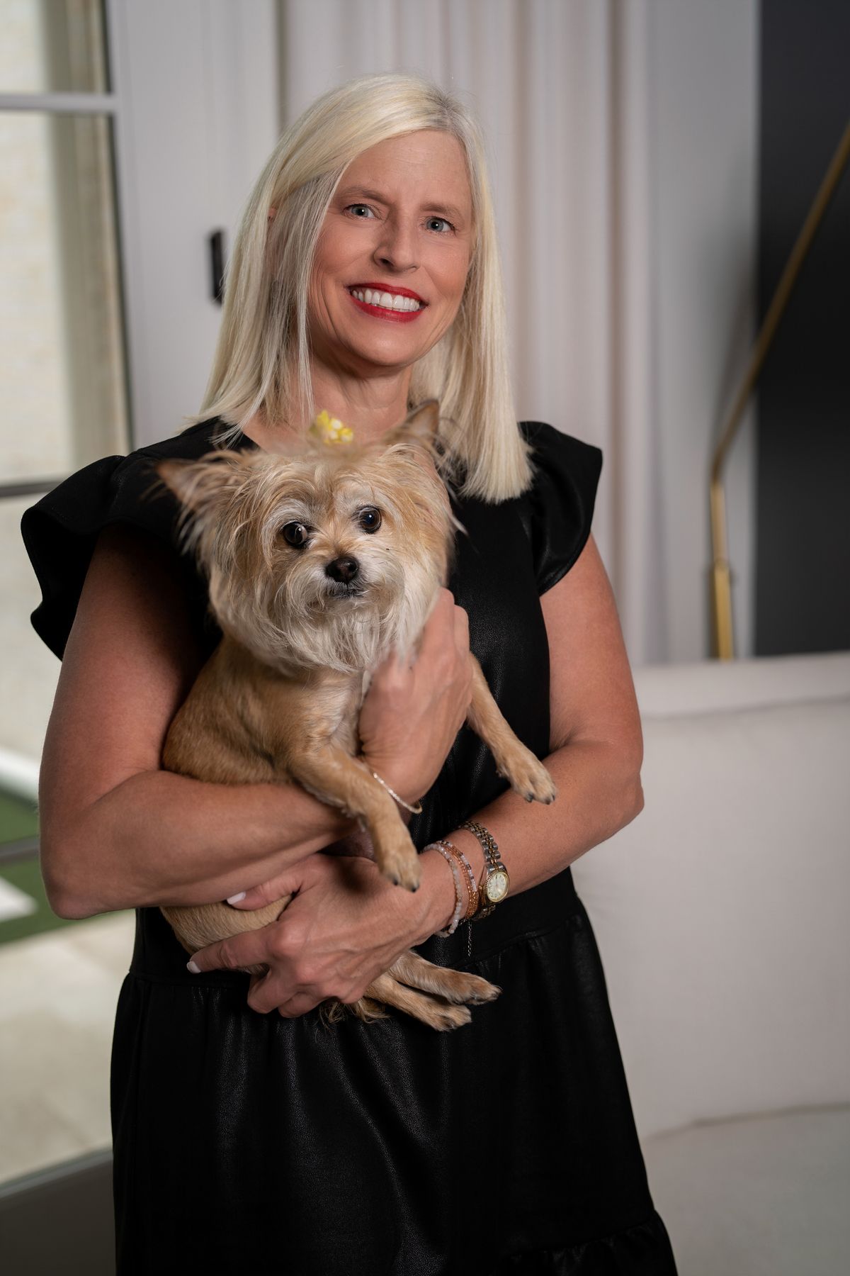 Michelle Creamer in a black dress, smiling and holding a small tan dog