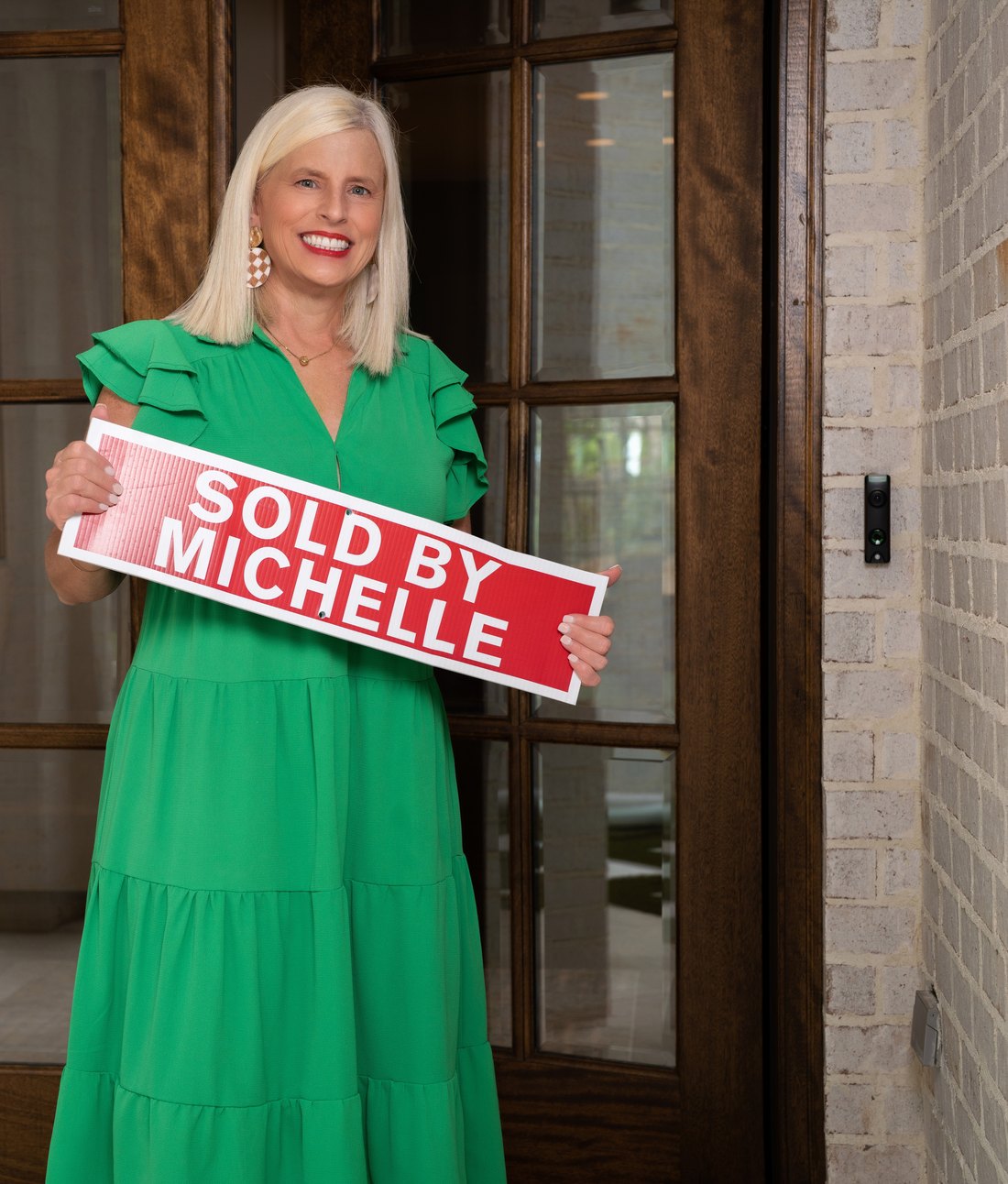 Michelle Creamer in a green dress holding a Sold by Michelle sign
